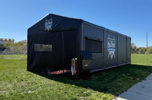 The Premium Hit House set up on a grass field with bats racked at the door