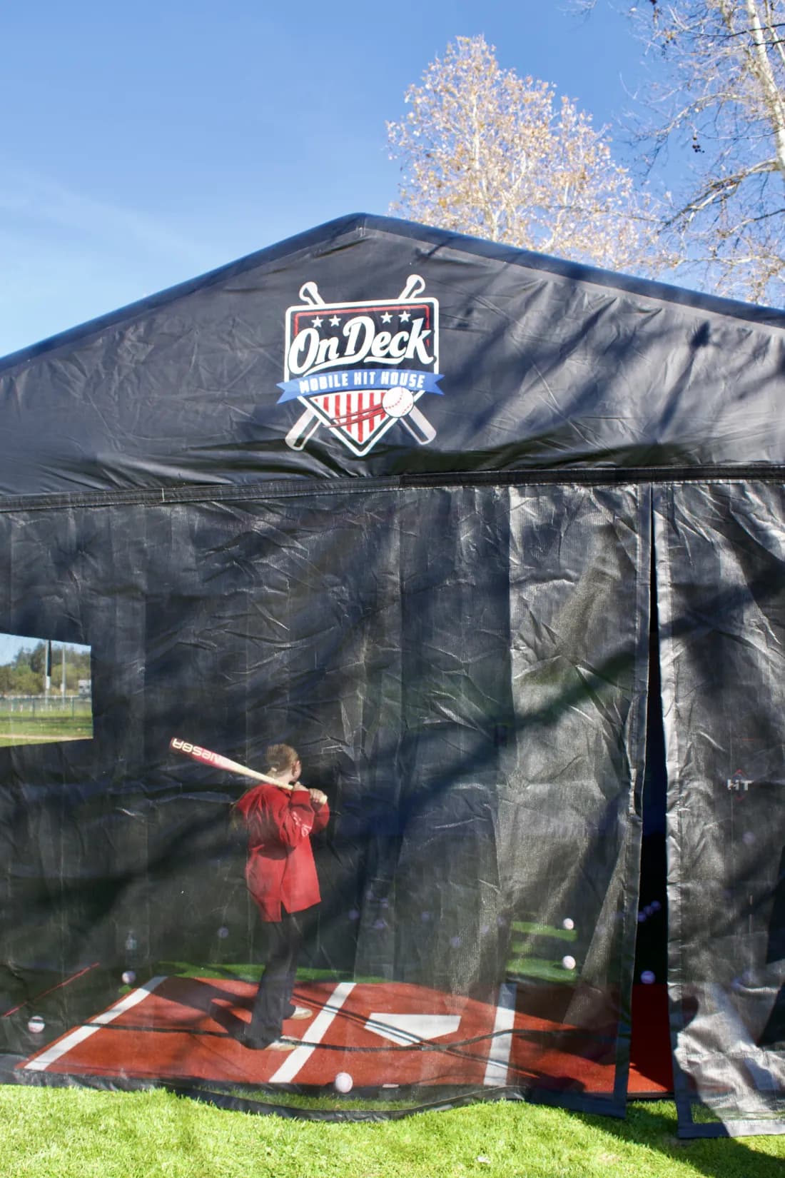 A player mid-swing inside the On Deck hit house at an outdoor event